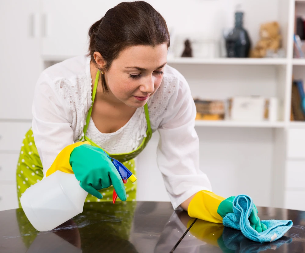 Woman in gloves scrubbing a table with a spray bottle.