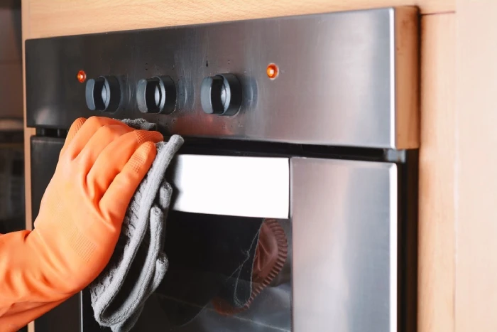 Gloved hand wiping clean a stainless steel oven.